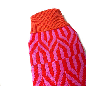 Hot water bottle with hand knitted cover in a geometric pink and red pattern.