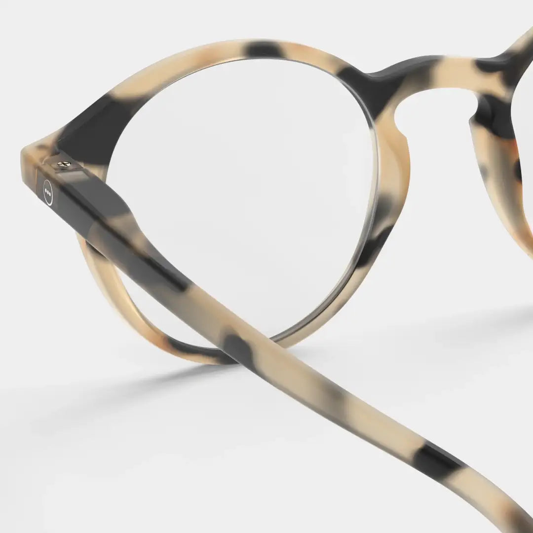 Close up of circular-shaped reading glasses in light tortoise colour against white background.