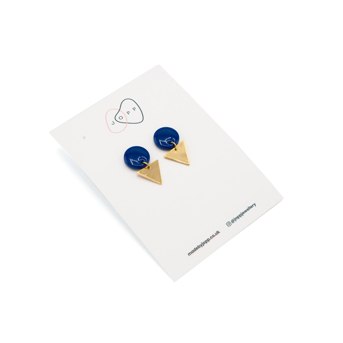 Earrings with a blue circle at the top, attached to a gold triangle underneath. Photographed against Jopp branded backing card.