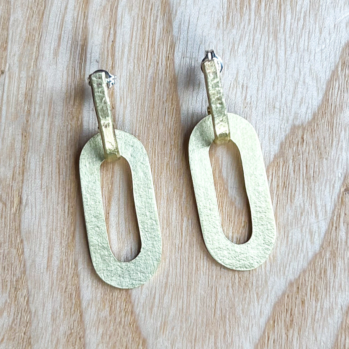 A pair of gold oval earrings with a hollow centre and textured posts.