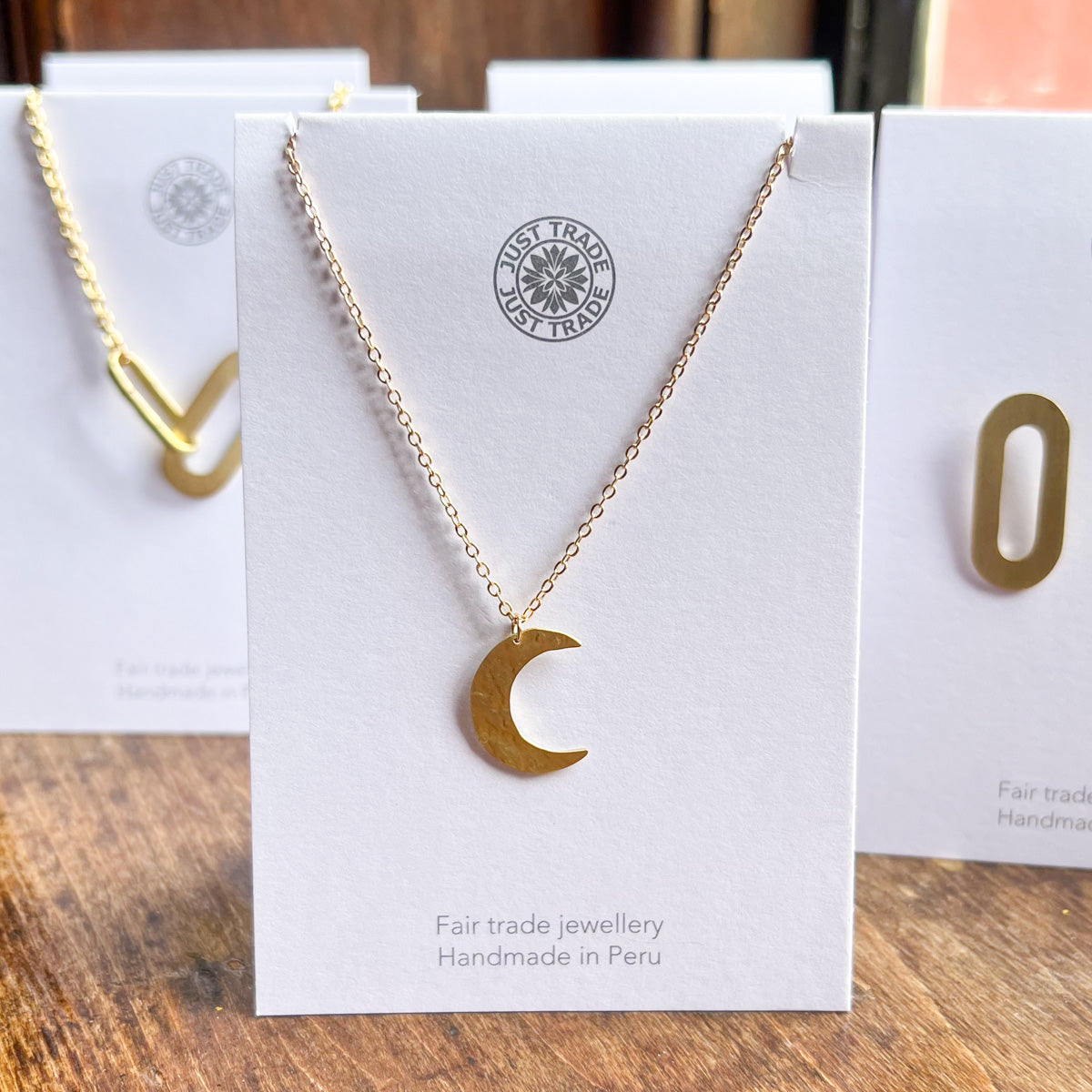 A gold crescent moon necklace on a card with the Just Trade logo on it.