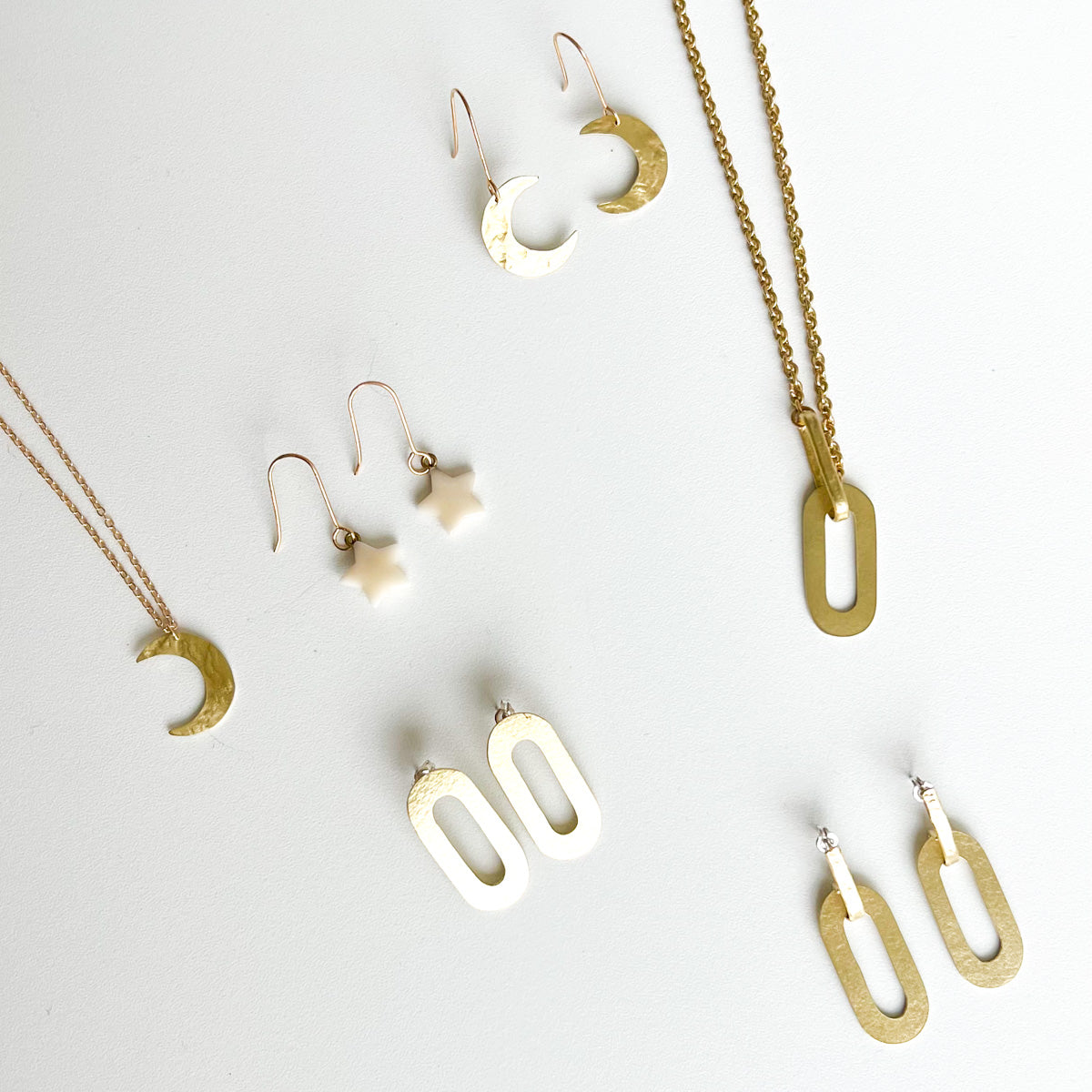 A collection of gold jewellery including crescent moon earrings, a crescent moon necklace, a star-shaped earring pair, a rectangular pendant necklace, and a pair of rectangular earrings.