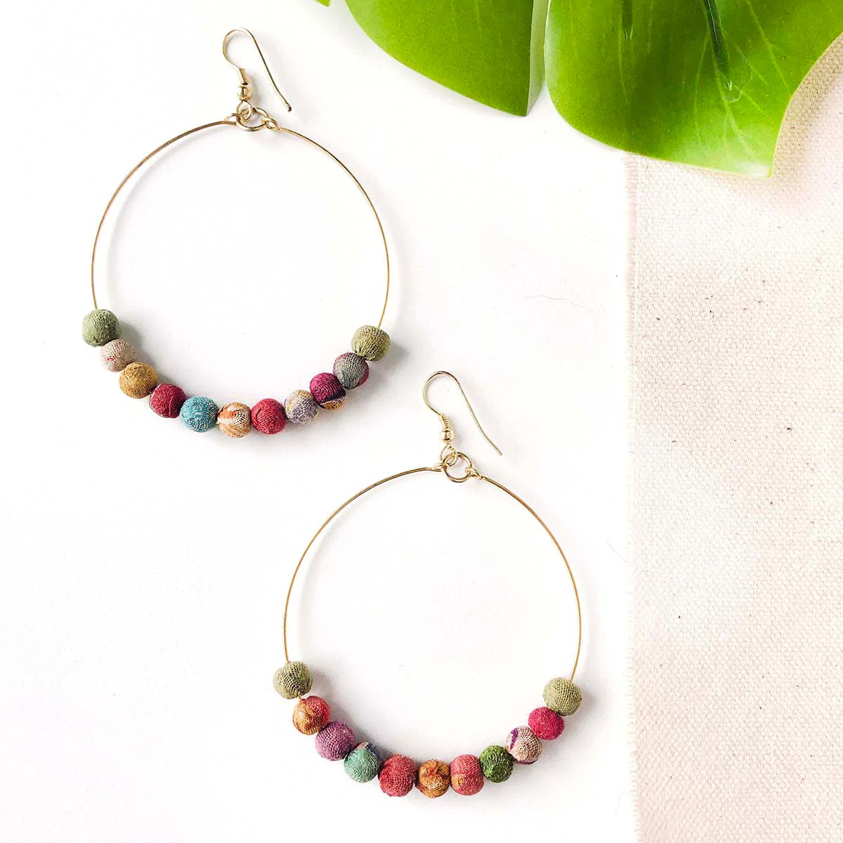 A pair of colourful hoop earrings with small fabric beads in various shades of pink, purple, and orange.