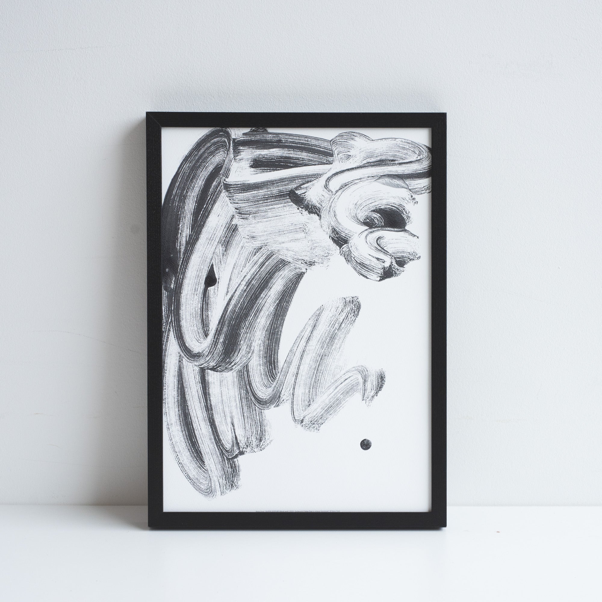 Printed reproduction of a unique Monotype by Kevin Hunt, placed in a black frame leaning against a white wall.