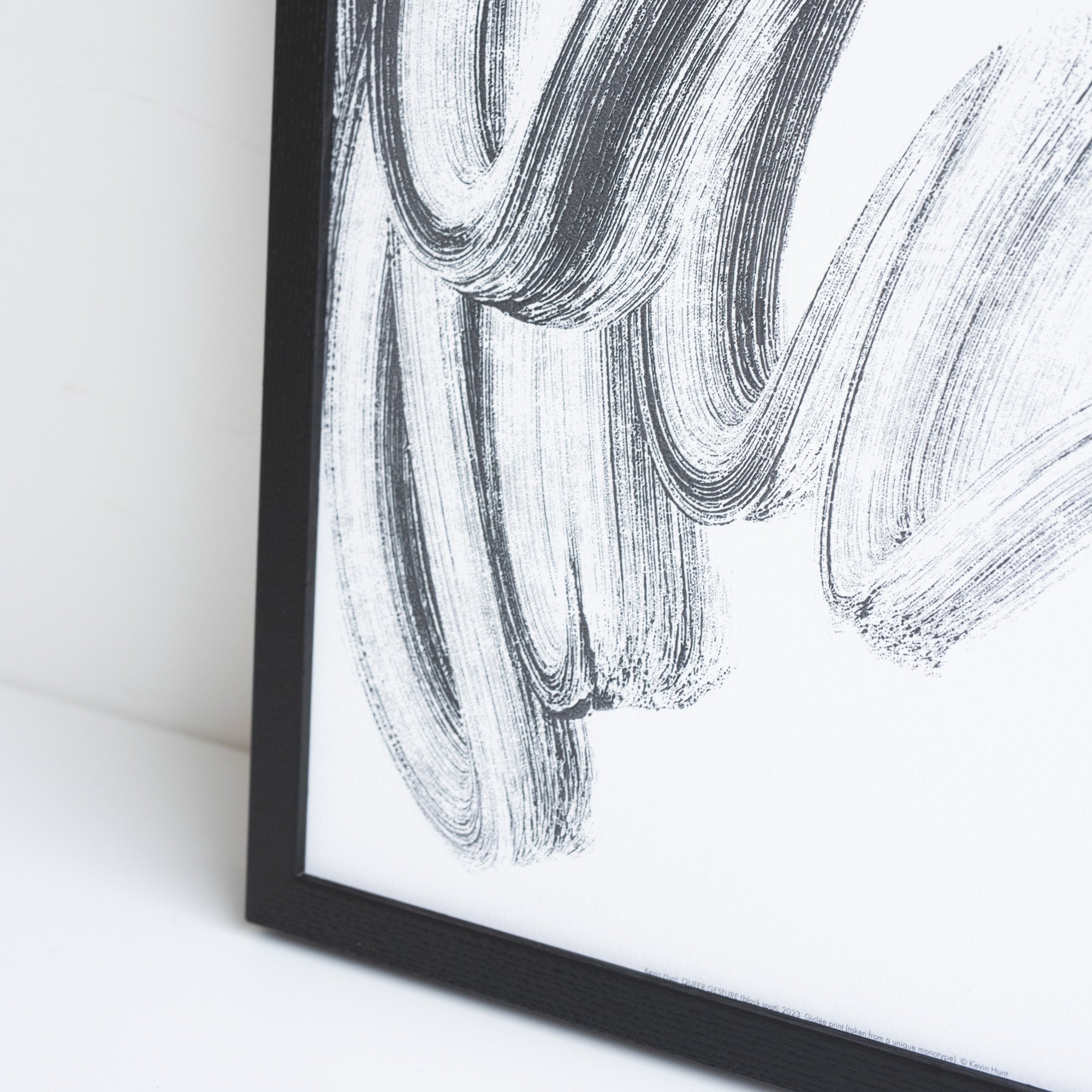 Close up of a printed reproduction of a unique Monotype by Kevin Hunt, placed in a black frame leaning against a white wall.