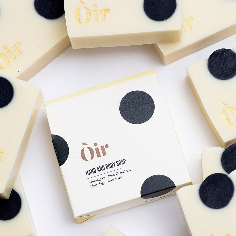 The image shows packaging for hand and body soap. It has a cream and black circles design. Surrounded by soaps. Photo taken from above.