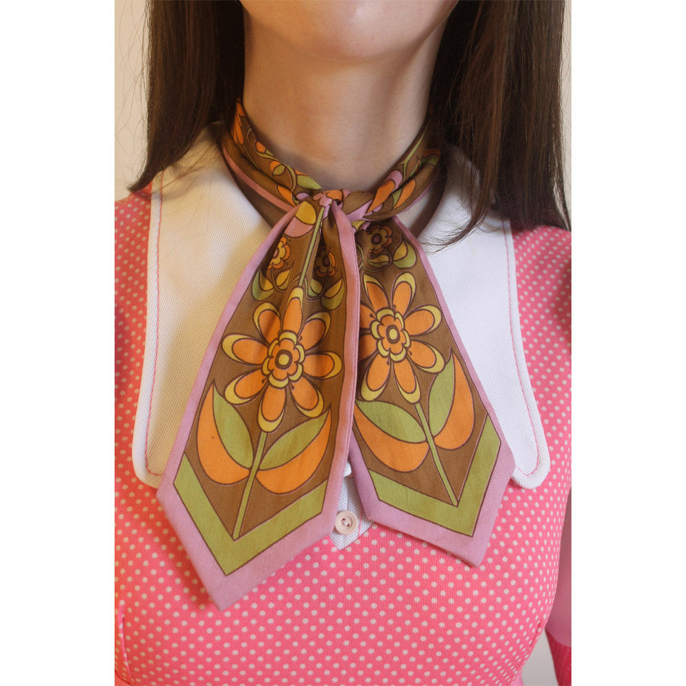 Person wearing a floral patterned scarf with a white blouse and pink polka dot dress.