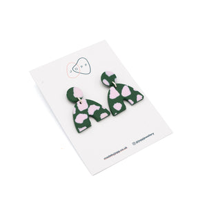 Earrings in a horseshoe shape photographed on top of backing card with Jopp branding. The earrings have a green and light pink cow print pattern.