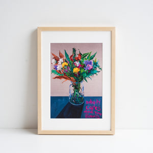 Print reproduction of a painting of some flowers by Michelle Taube, placed in an ash frame resting against a white wall