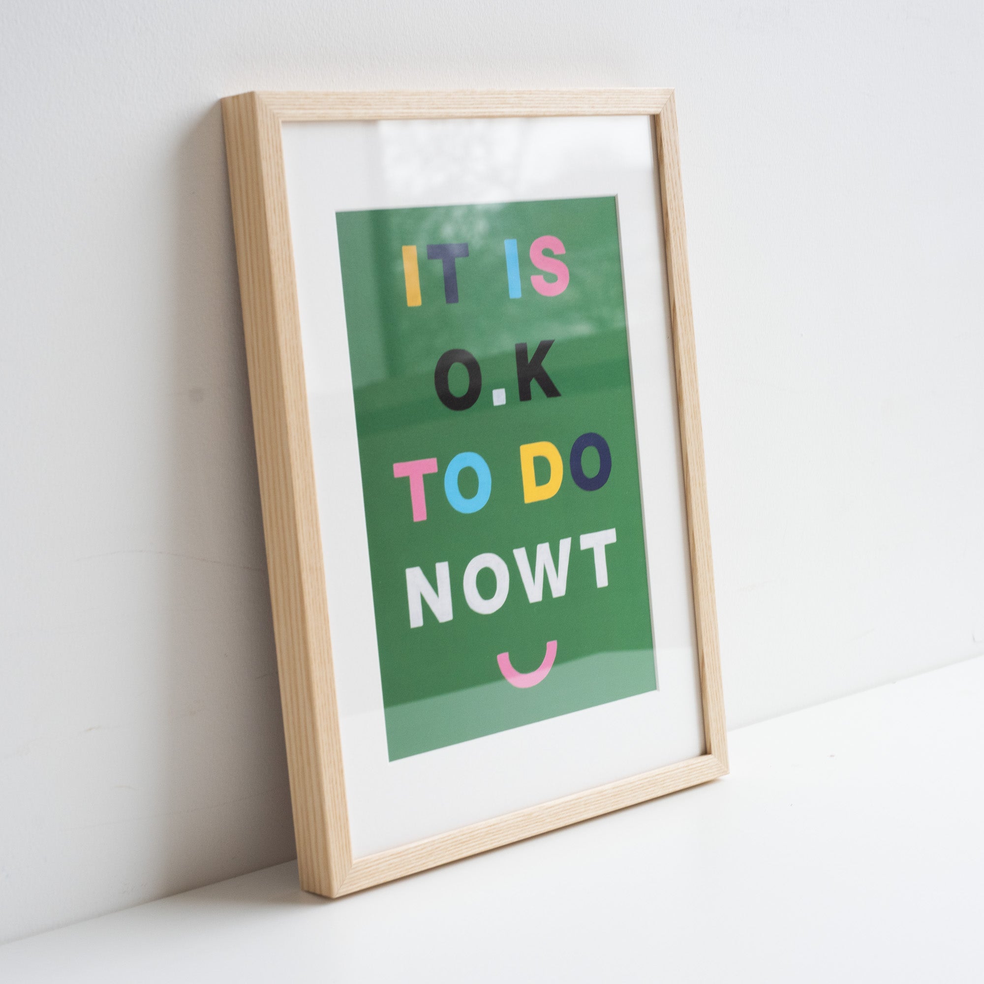Artwork by Mikesian studio in an ash frame, rested against a white wall. Green background with colourful typography
