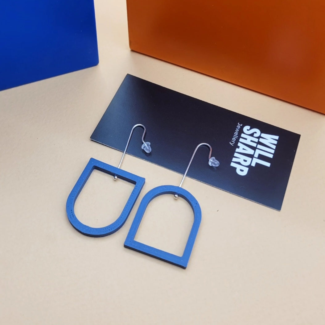 Blue archway shaped 3D printed earrings on a beige background with black branded backing card.