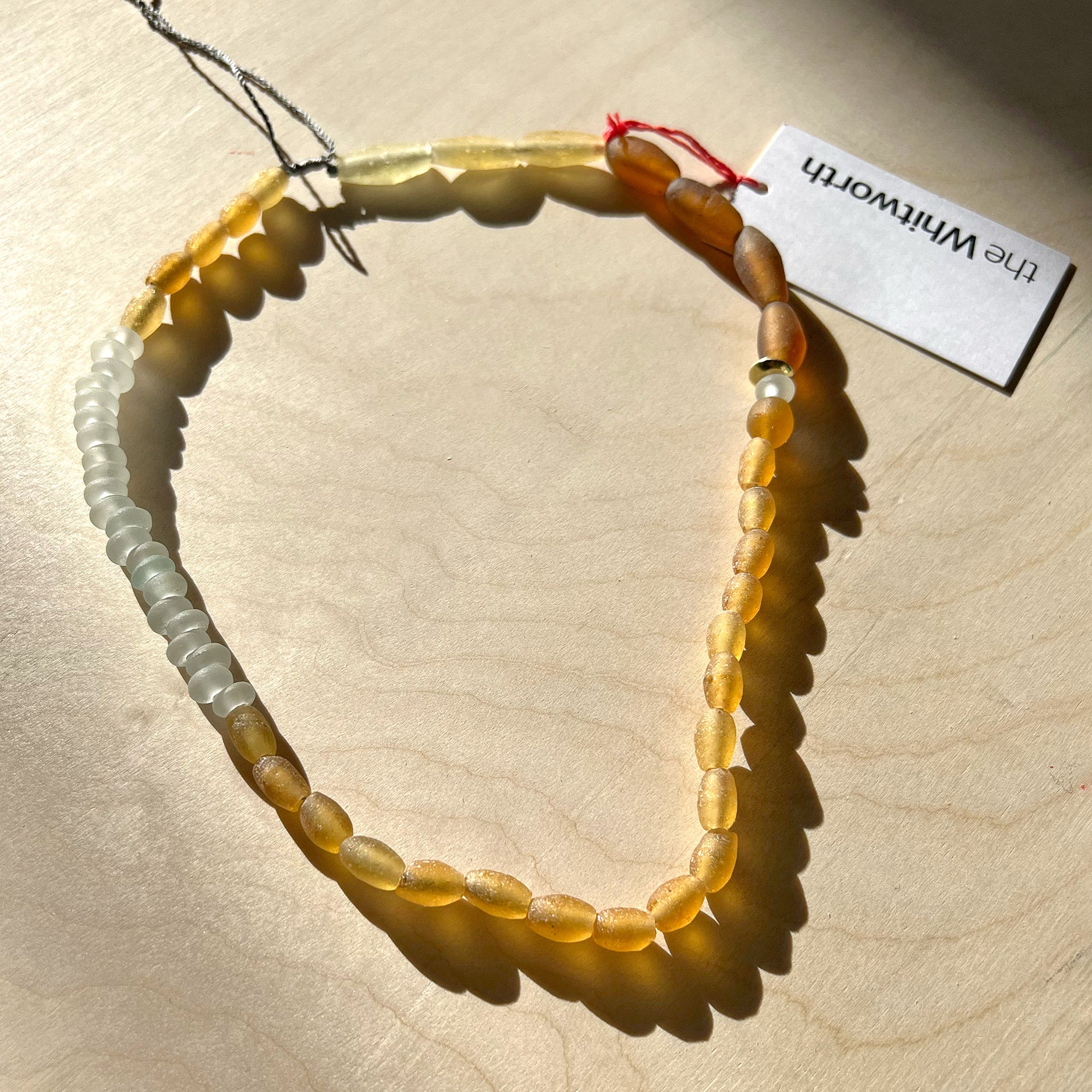 Orange & brown glass beaded necklace presented on a wooden surface in the sunlight.