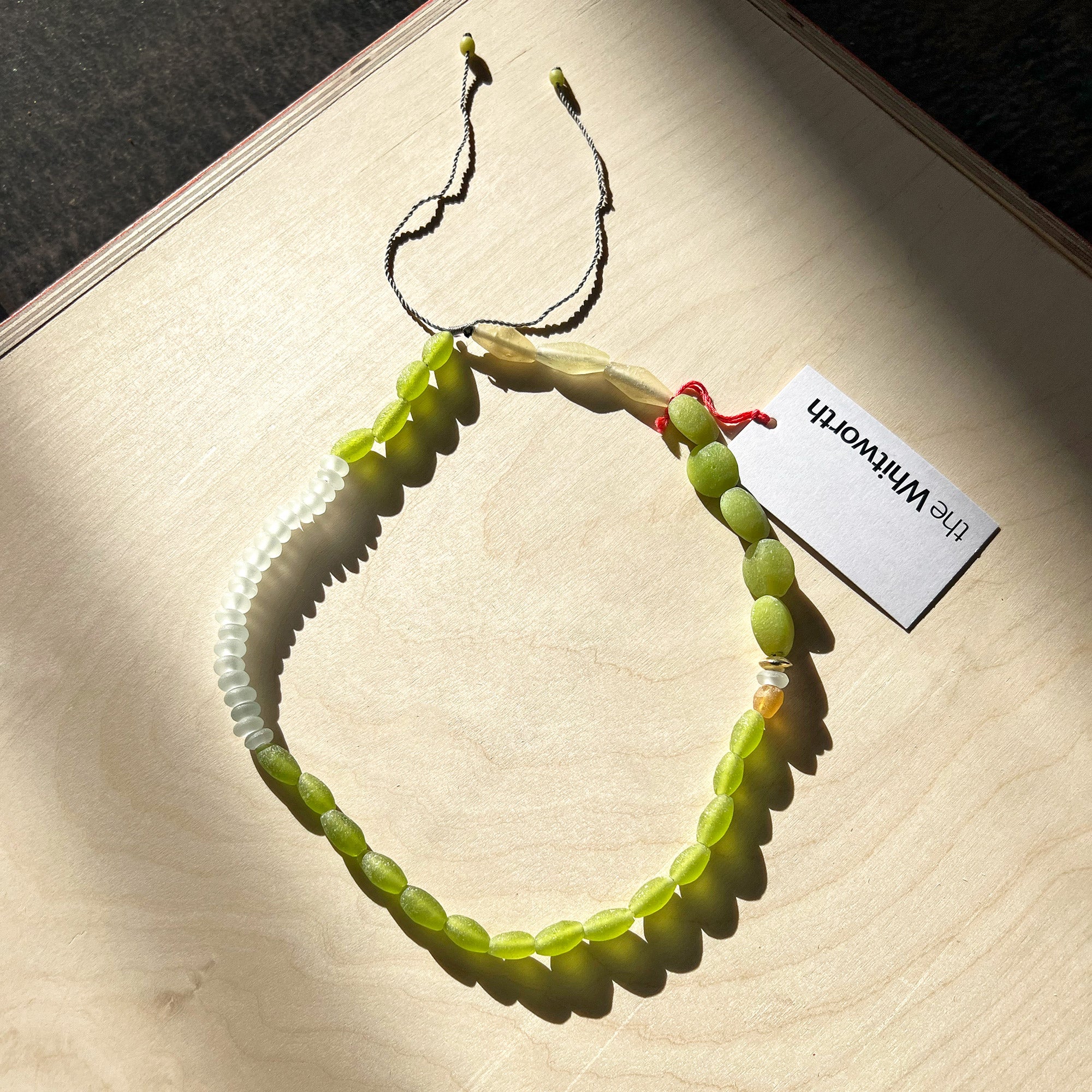 Green glass beaded necklace presented on a wooden surface in the sunlight.