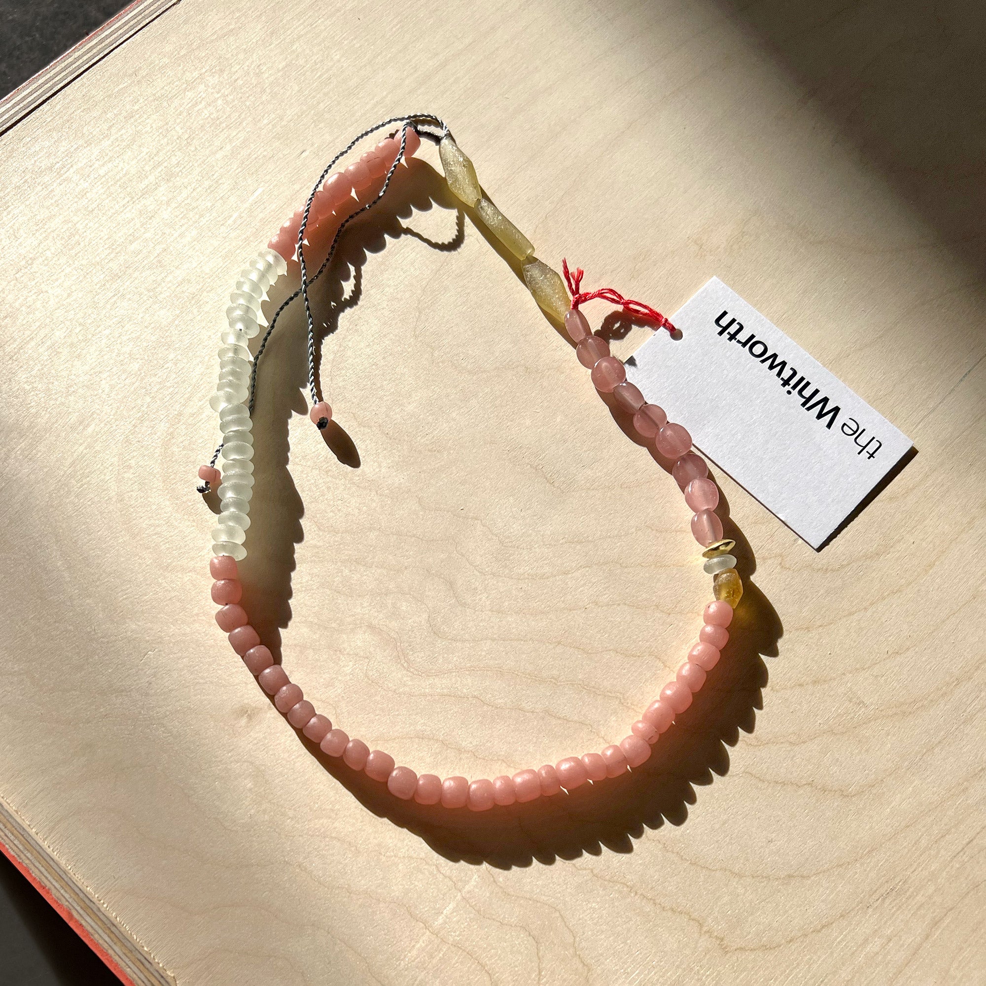 Pink glass beaded necklace presented on a wooden surface in the sunlight.