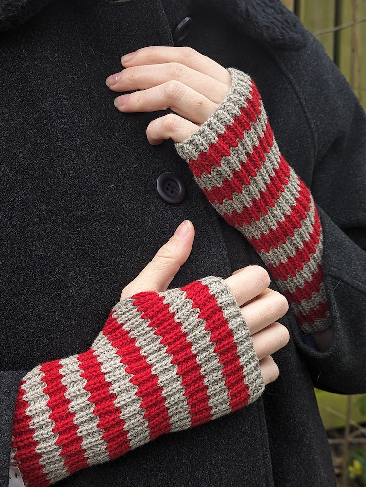 A person wearing red and grey striped knitted fingerless gloves. 