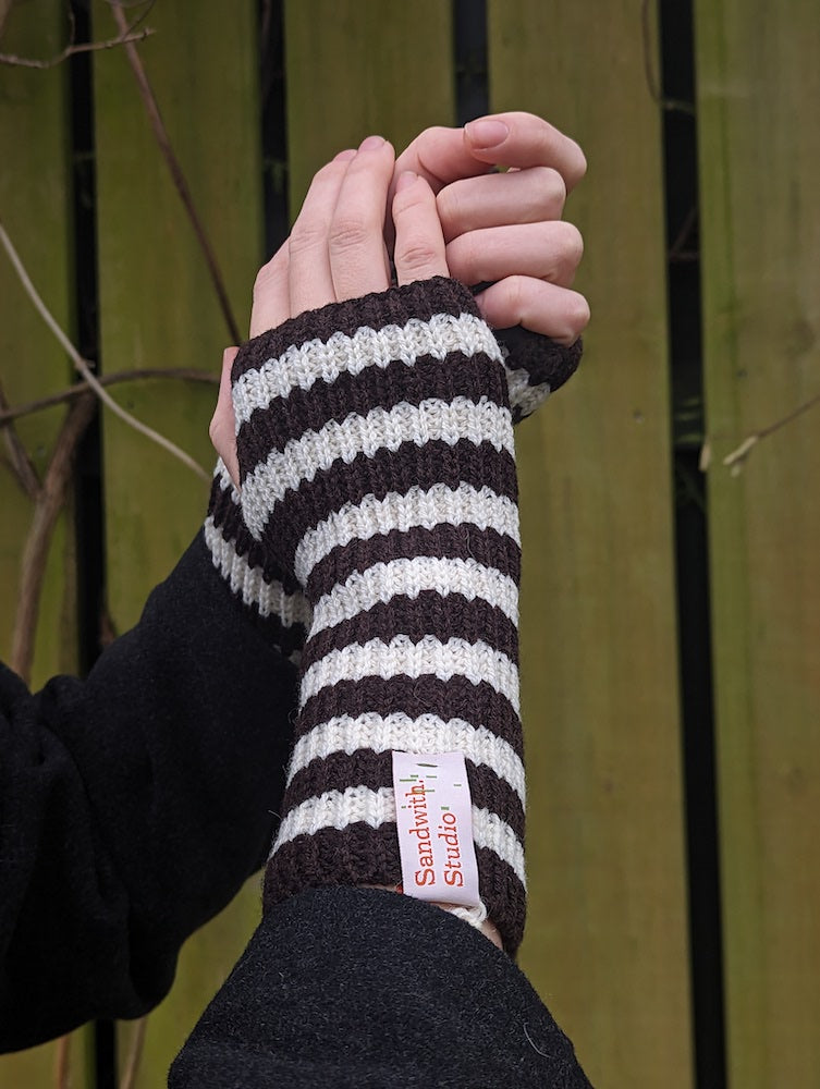 A person wearing brown and grey striped knitted fingerless gloves.