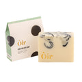 A bar of Oir Hand and Body Soap in a Peppermint, Lavender, Patchouli, and Tea Tree scent sits on a white background next to its packaging.