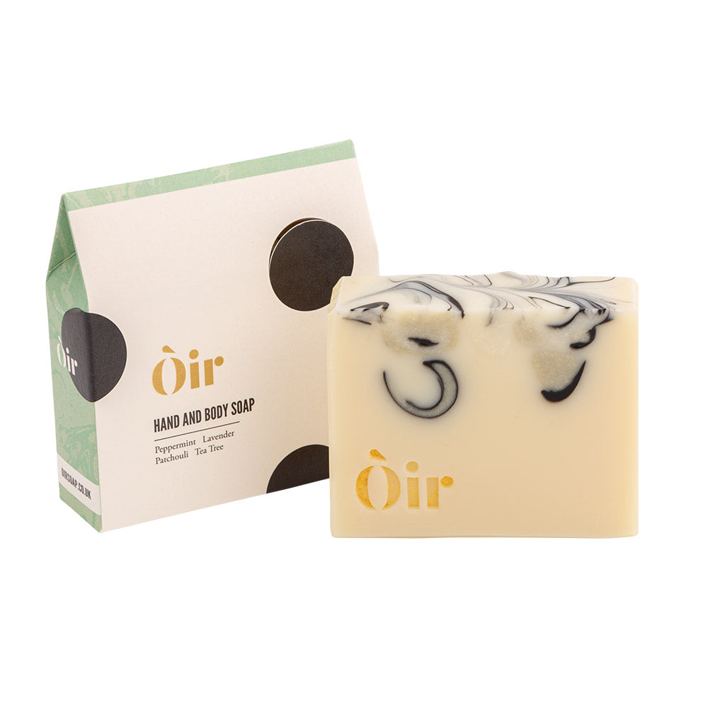 A bar of Oir Hand and Body Soap in a Peppermint, Lavender, Patchouli, and Tea Tree scent sits on a white background next to its packaging.