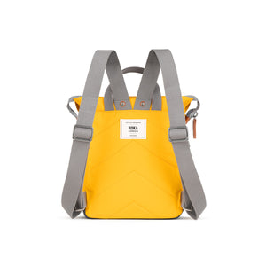 A yellow backpack with grey straps. The backpack has a roll-top closure and a ROKA London logo on the back.