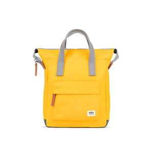 A yellow backpack with grey handles and straps. The backpack has a zip closure, a small front pocket, and a ROKA London logo on the front.