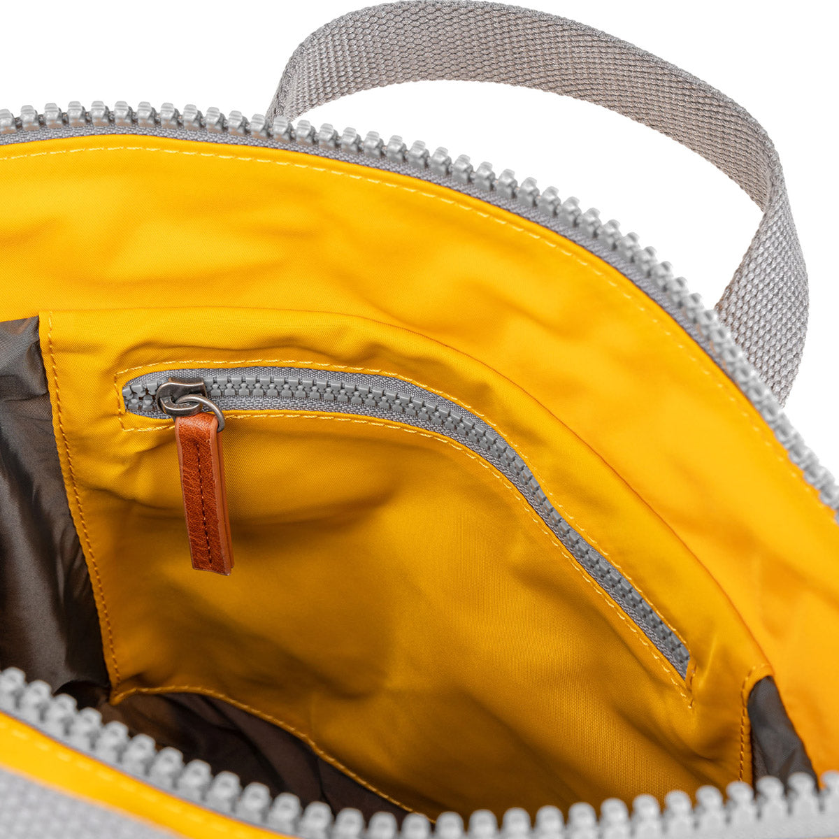 The inside of a yellow backpack with a gray zippered pocket and a brown leather pull tab. The lining is also yellow.