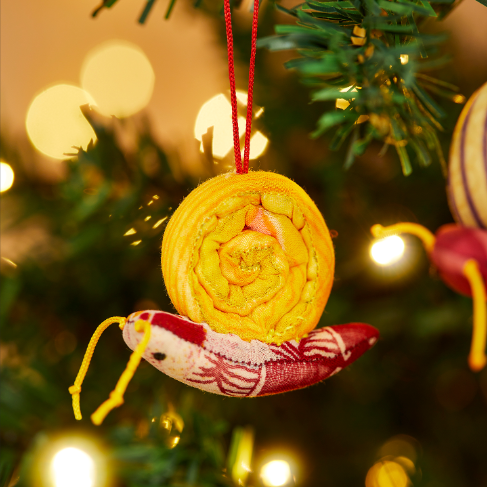 Snail made out of recycled sari in yellow and red colours hanging on a Christmas tree.