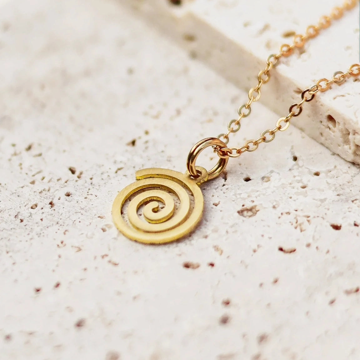 Gold necklace with a spiral pendant on a grey surface