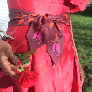 Person wearing a red dress with a decorative scarf holding a red rose.
