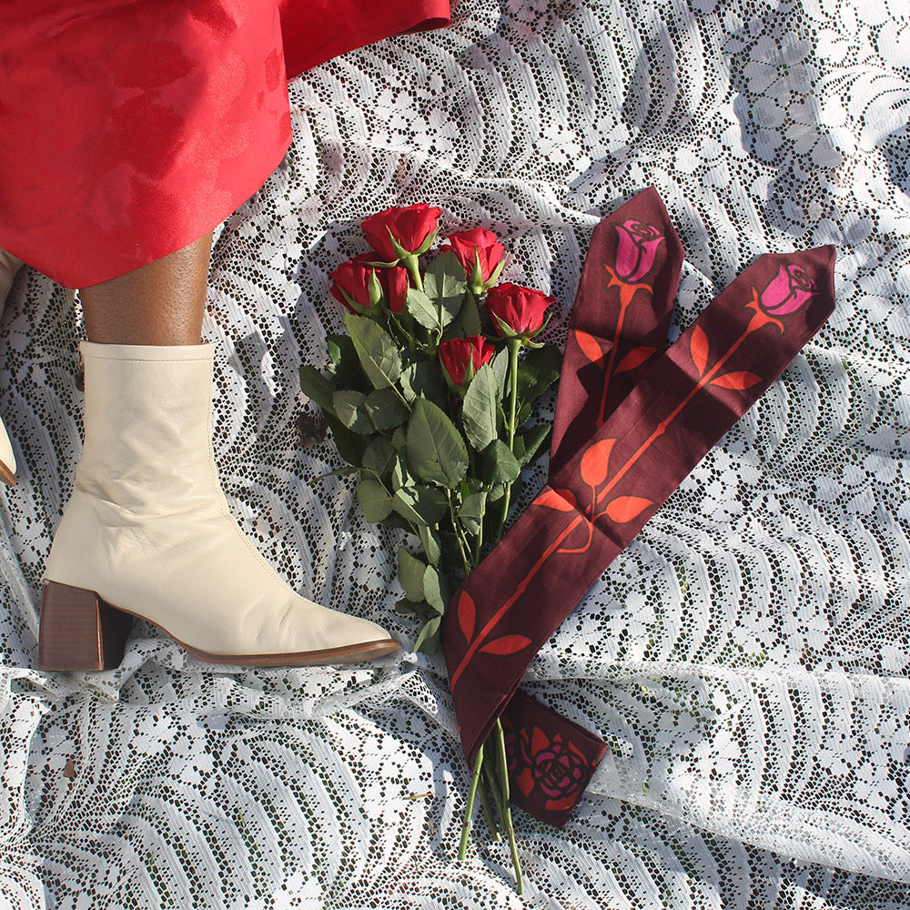 White ankle boots next to red roses on a lace surface