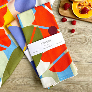 A folded tea towel with a bold, abstract design is presented on a tabletop surface.