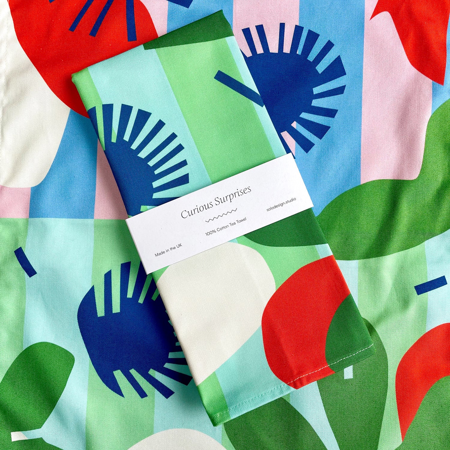 A folded tea towel with a bold, abstract design is presented on a surface with a similar pattern.