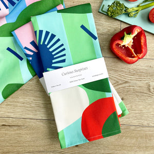 A folded tea towel with a bold, abstract design is presented on a tabletop.