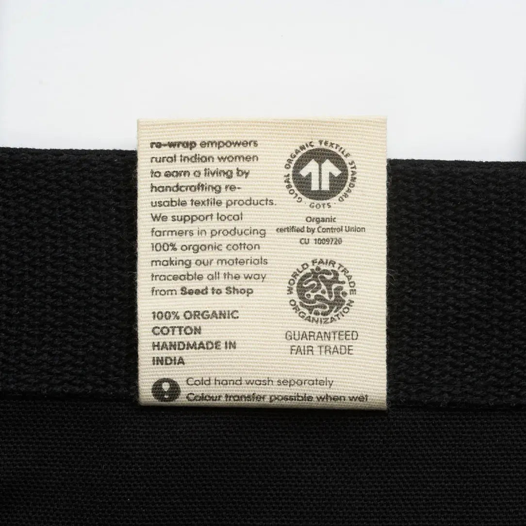 Label on the inside of a black fabric tote bag with text about organic cotton and fair trade certification.