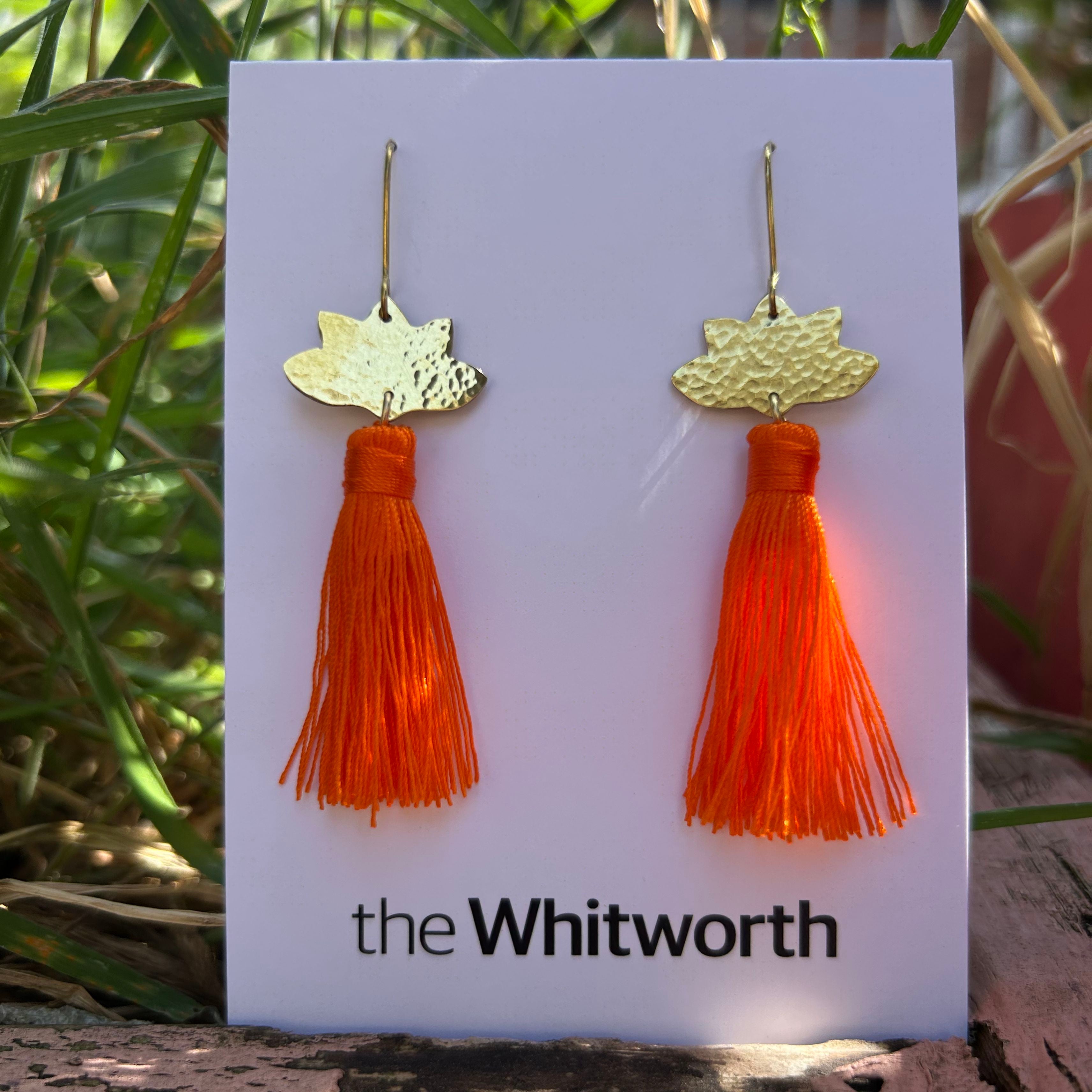 Orange tassel earrings on a 'the Whitworth' branded card with a natural background.