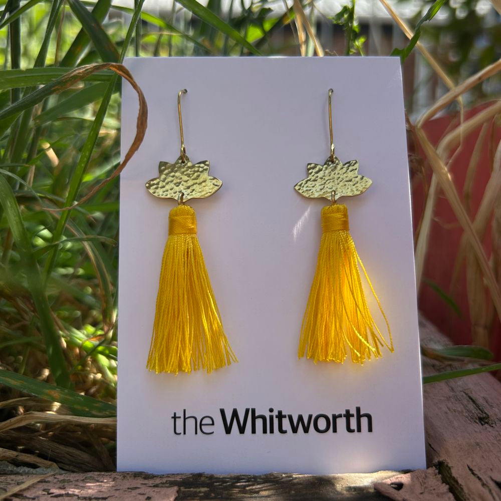 Yellow tassel earrings on a card with 'the Whitworth' branding, set against a natural background.