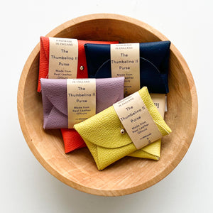 Multiple rectangular leather purses in various colours presented in a wooden bowl against a white background.