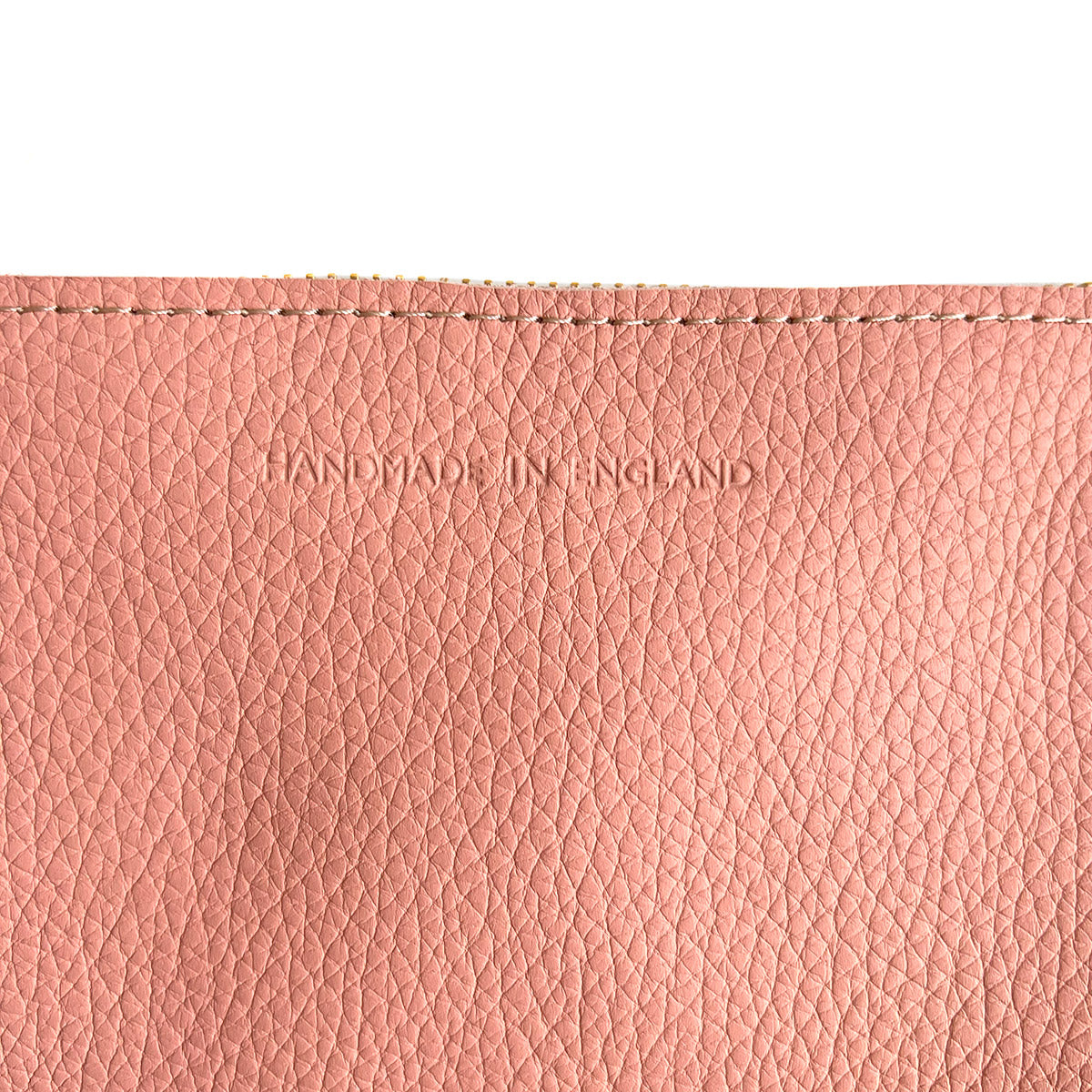 Detail of pink leather bag featuring gold zip and 'Handmade in England' embossed lettering.