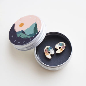 A pair of wooden artist's palette-shaped earrings inside a small round tin.