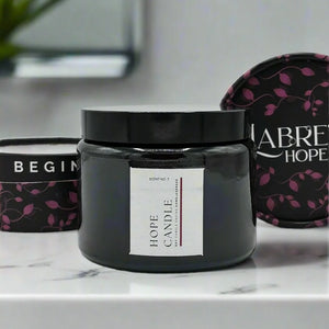 A black glass candle jar with a white label featuring pink vines.