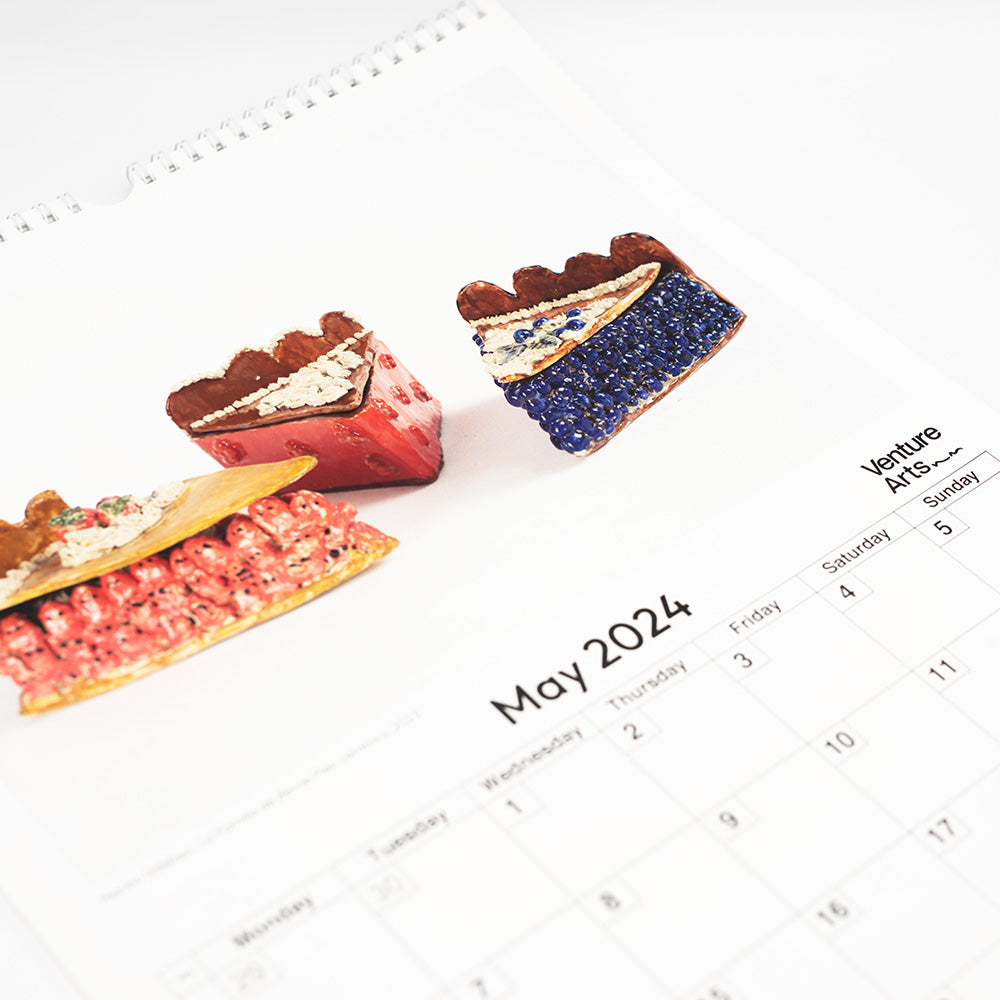 A close up of the May 2024 page of the calendar, featuring some ceramics in the shape of fruit pies