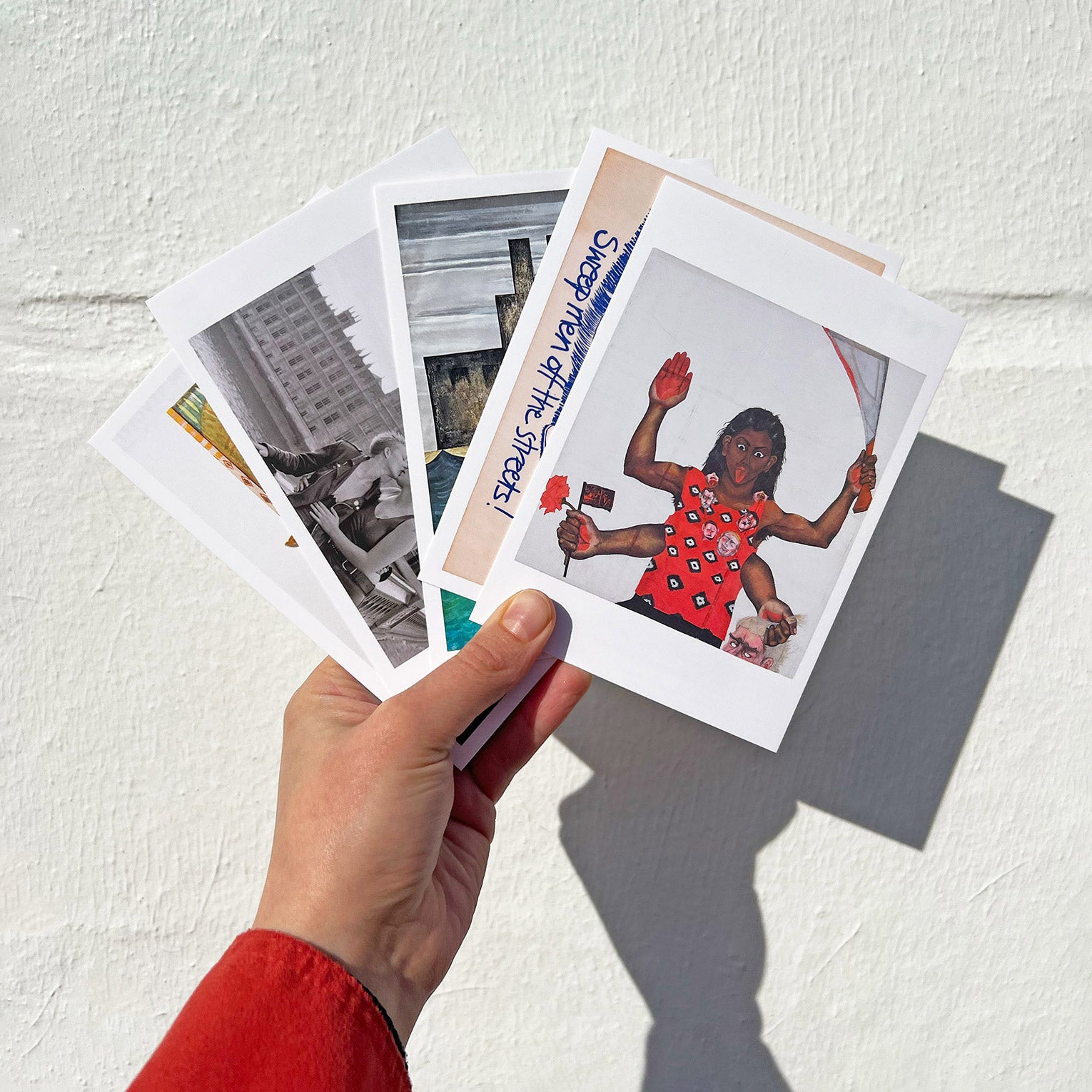 Someone holding up a series of Women in Revolt exhibition postcards in front of a white wall