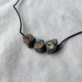 Necklace with three marbled stone-looking beads on a light grey fabric background