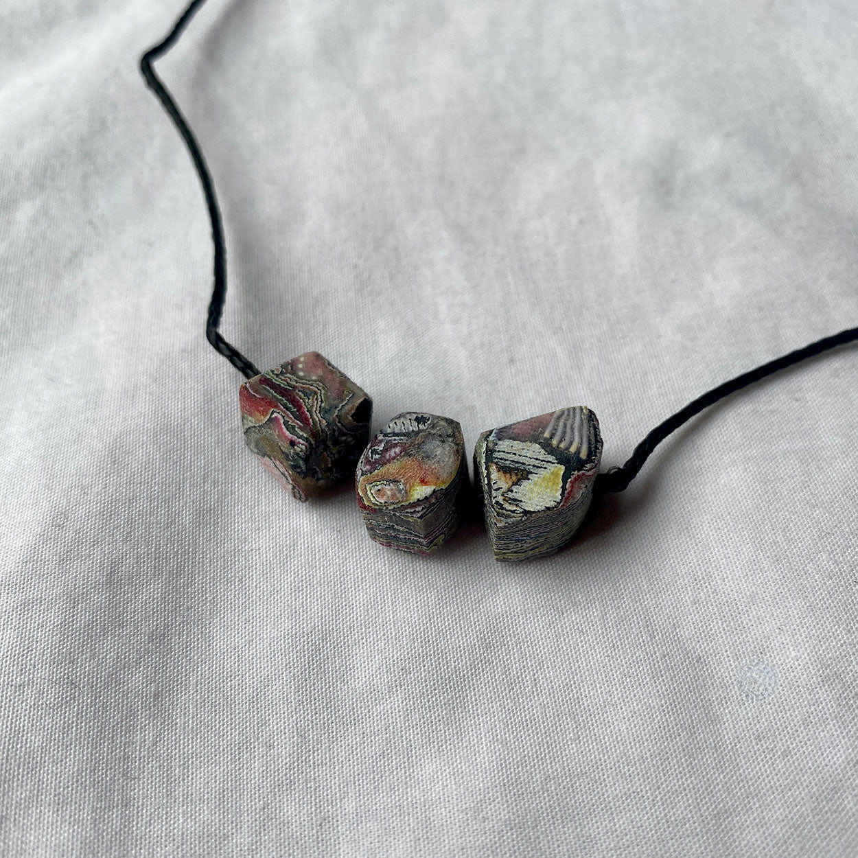 Necklace with three marbled stone-looking beads on a light grey fabric background