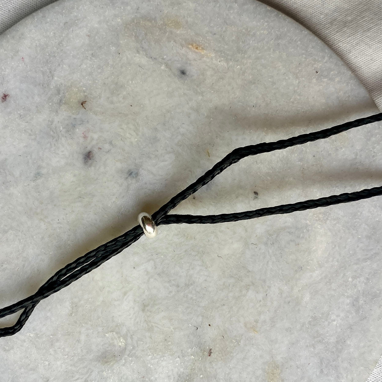 Black braided cord with a silver clasp on a textured gray surface