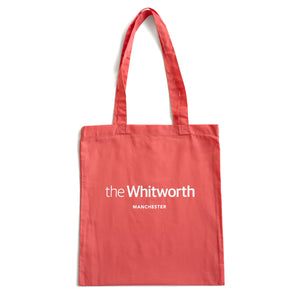 Coral coloured tote bag with Whitworth logo against white background.