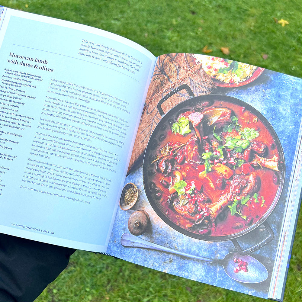 A person holding open a cookbook at a Moroccan Lamb recipe