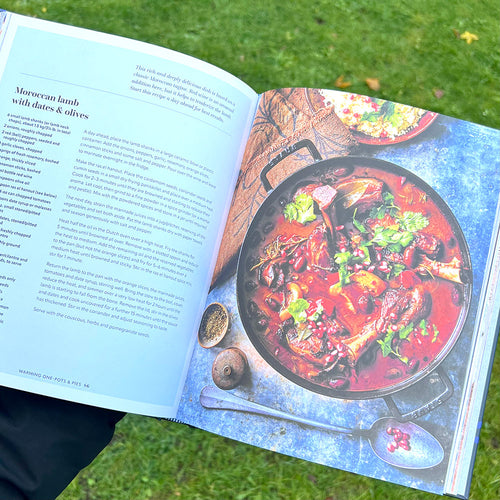 A person holding open a cookbook at a Moroccan Lamb recipe