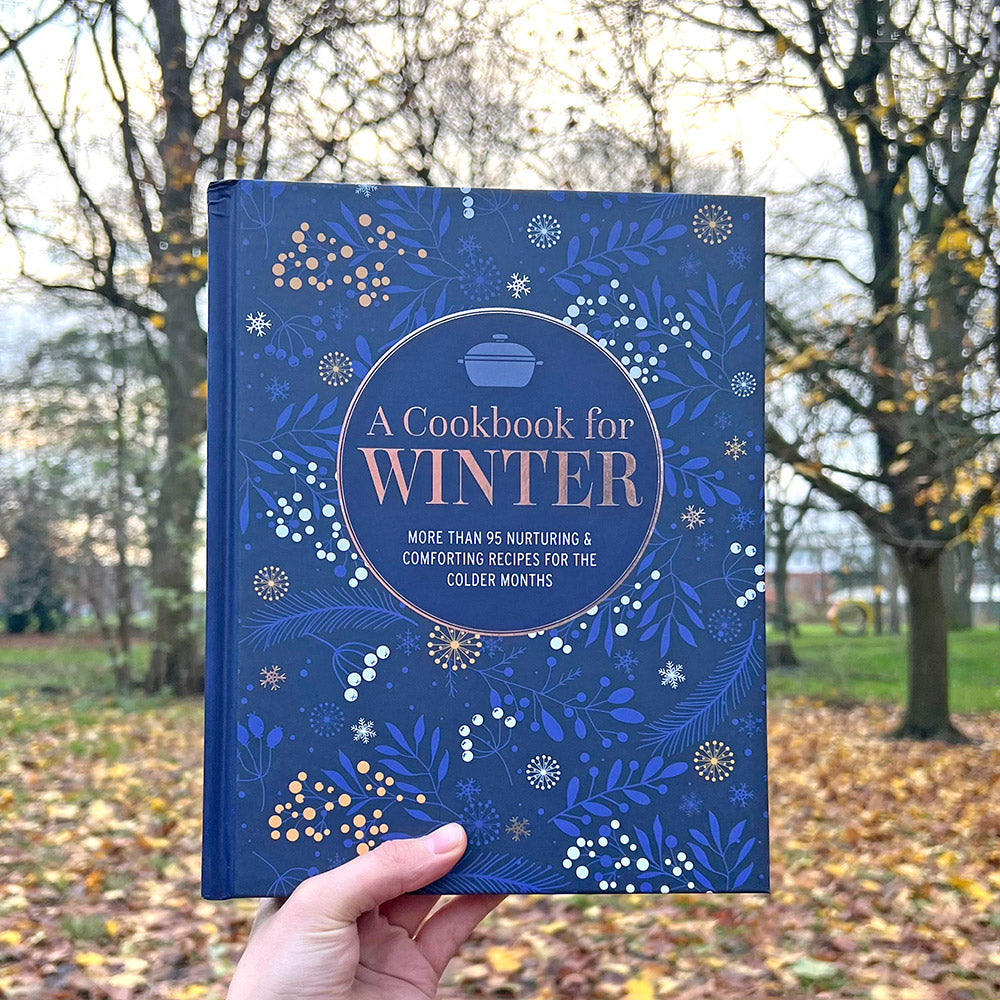 A person holding a blue cookbook in front of the Whitworth Park
