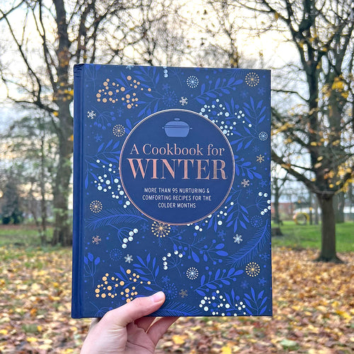 A person holding a blue cookbook in front of the Whitworth Park