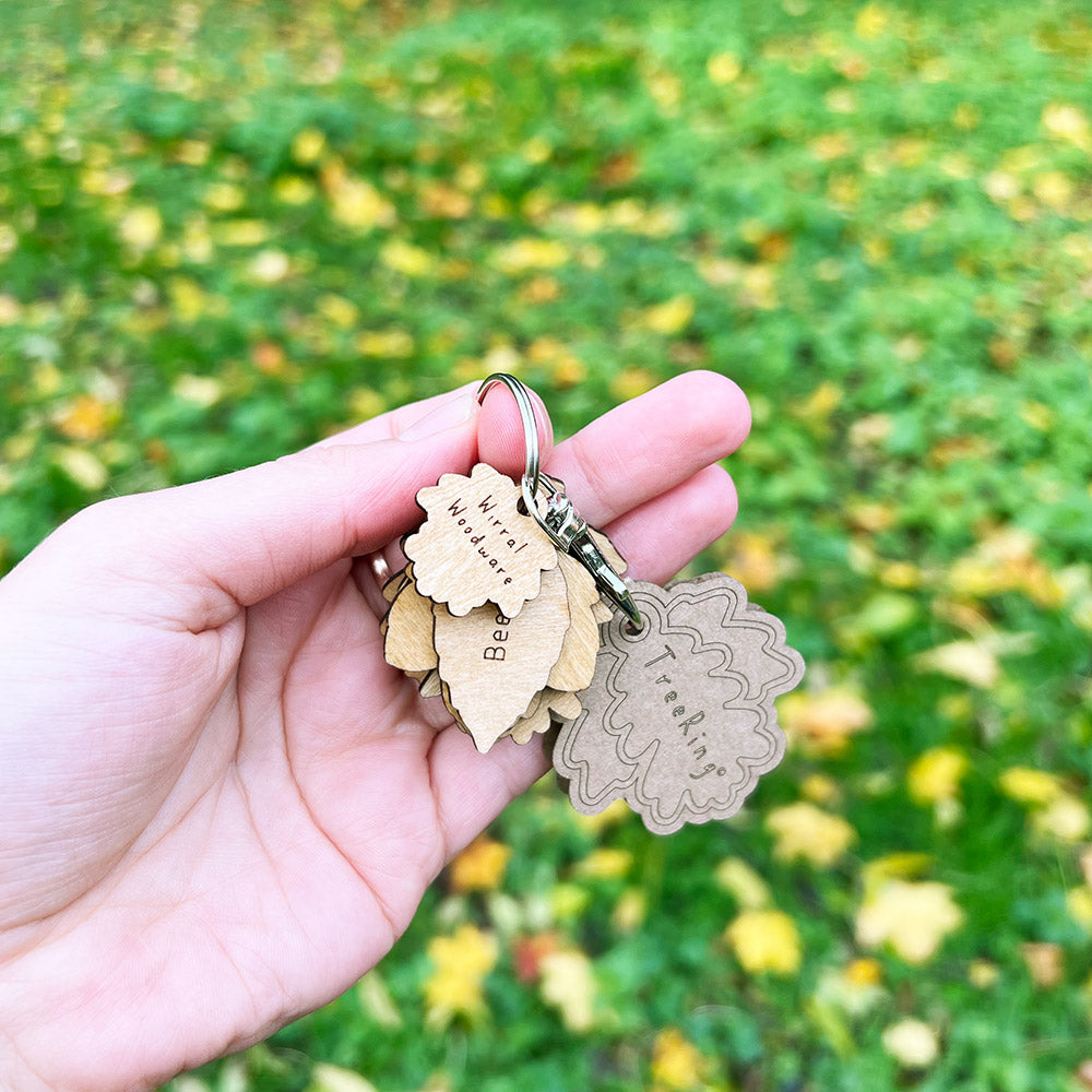 Hand holding a keychain with leaf-shaped tags against a blurred green and yellow background